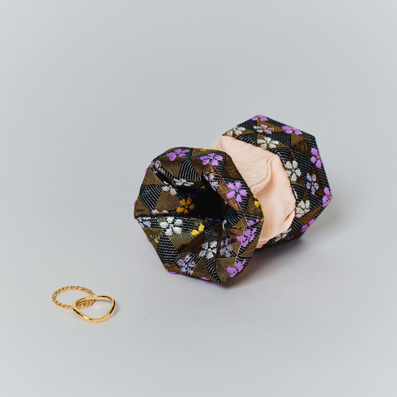 An open black and gold silk jewelry box placed next to gold rings, showcasing its use as a stylish accessory organizer.